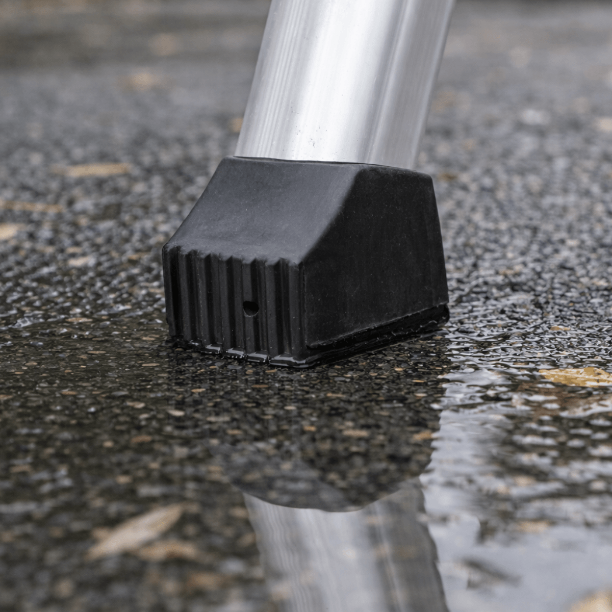Close-up of a black rubberized protective boot or guard attached to a silver metal pole, standing in wet asphalt with water puddling around it.