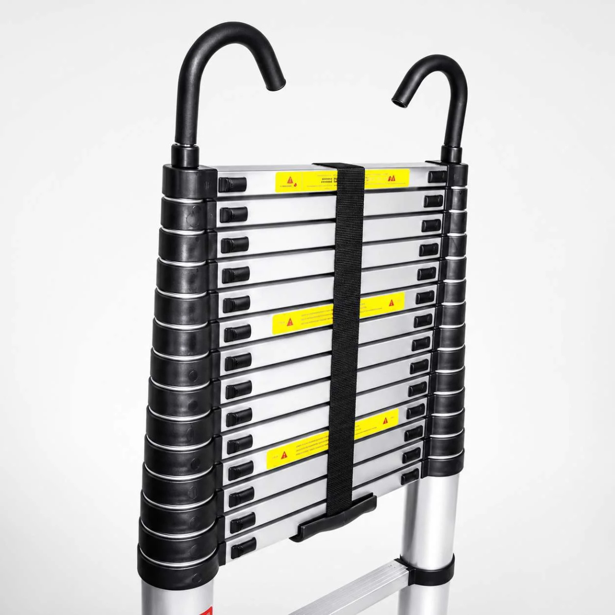 A close-up of a folding aluminum extension ladder showing the side panel with black rubberized grips, yellow warning labels, and black handlebar-like supports on a light gray studio background.